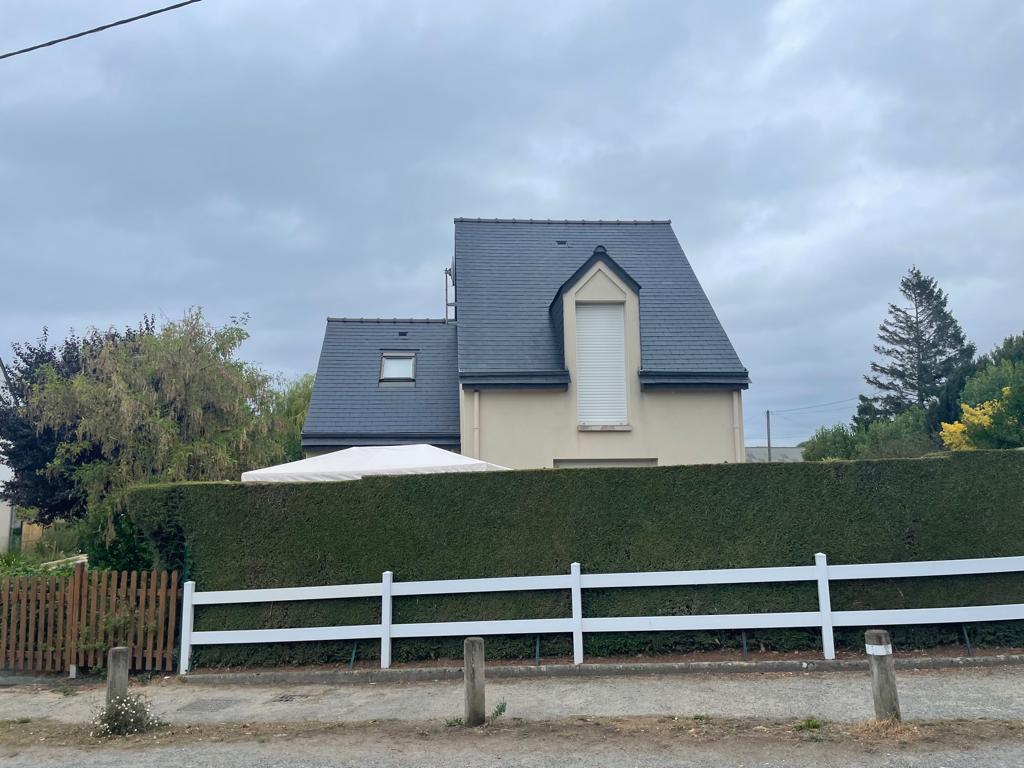 Maison avec clôture et haie verte.