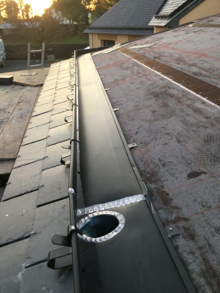 Installation de gouttières sur un toit en ardoise.