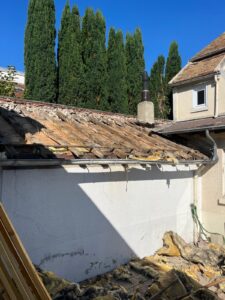 Toit ancien en rénovation avec arbres en arrière-plan.