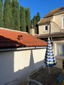 Cour avec parasol rayé et hauts arbres.